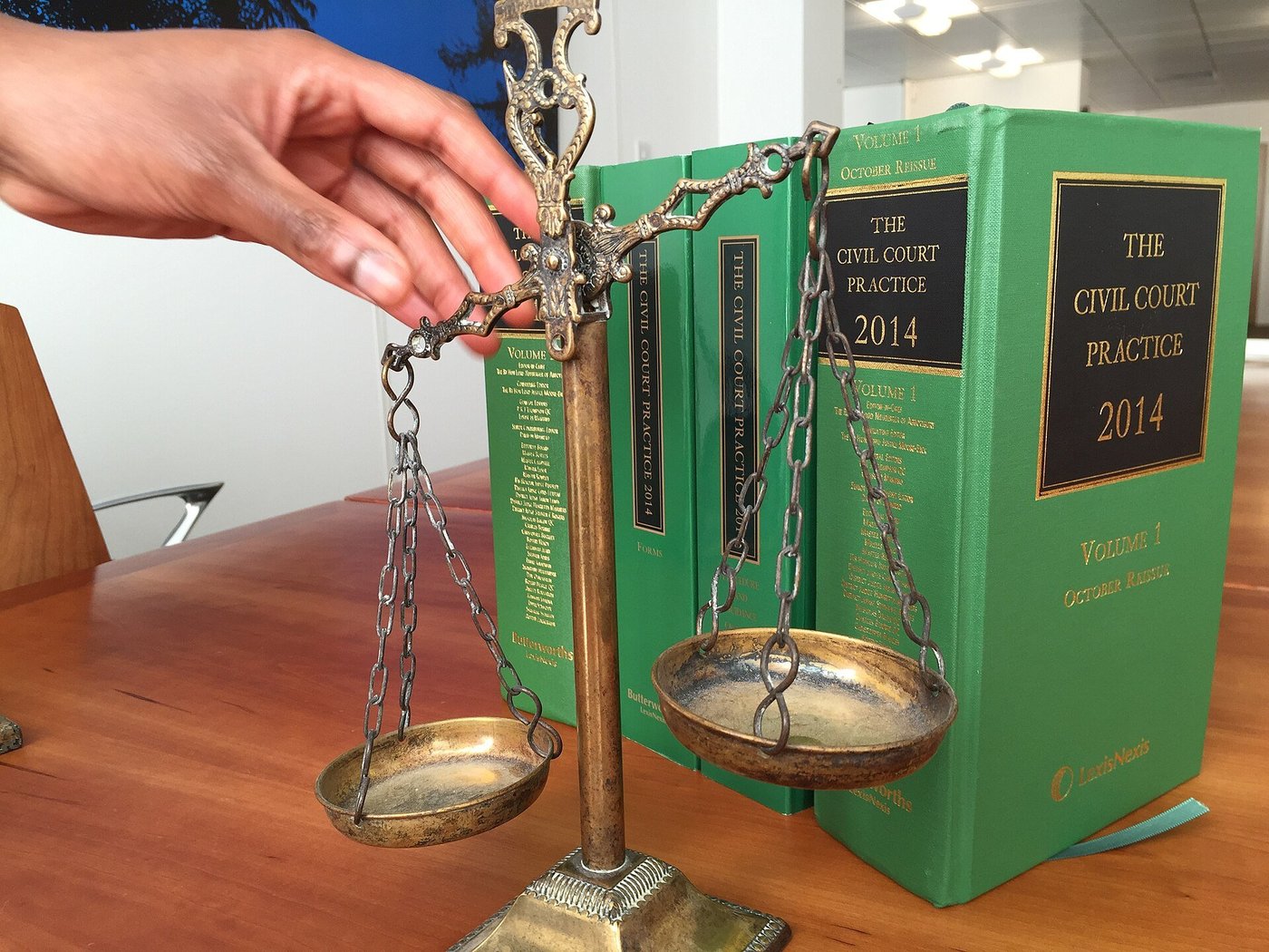 Een hand zet een weegschaal van justitie neer naast een groen boek over het burgerlijk procesrecht.