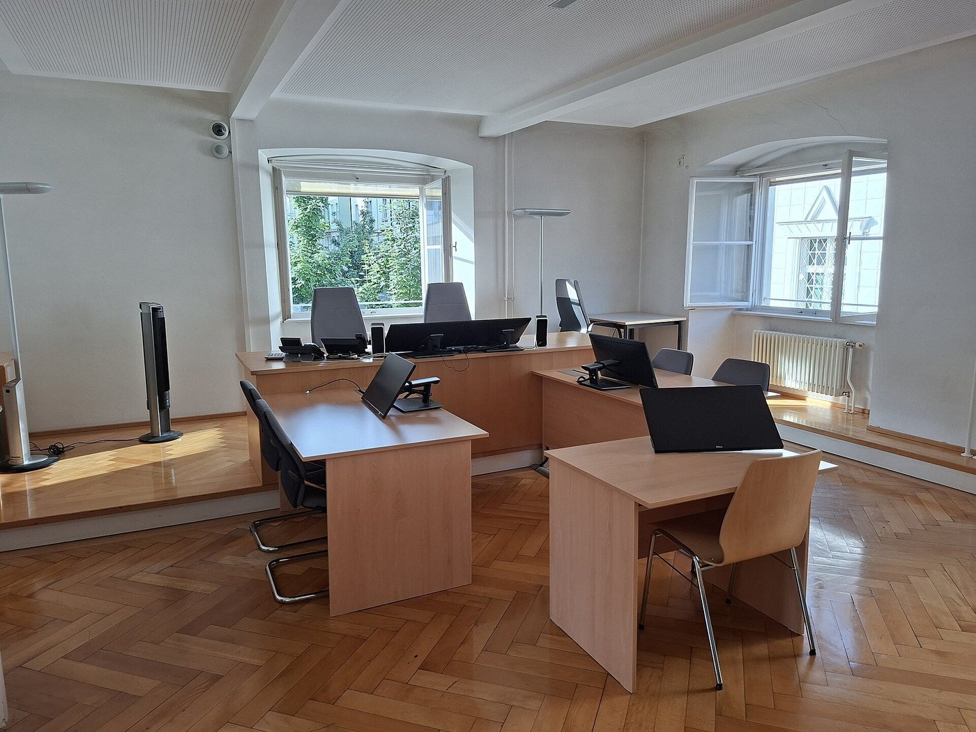 Een lichte rechtszaal met houten tafels en computerschermen, zonder mensen.