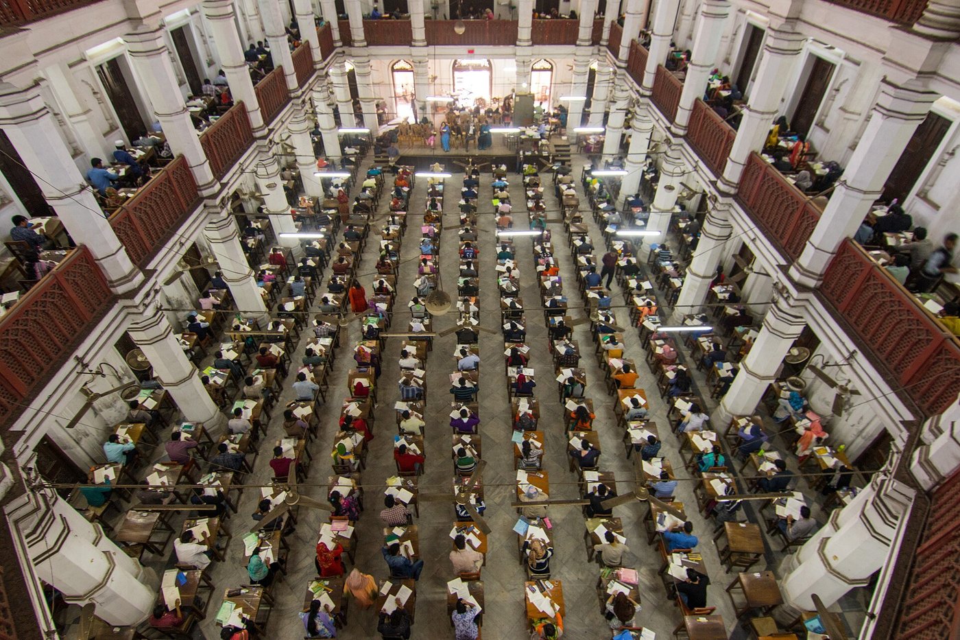 Een grote zaal vol kandidaten aan tafels tijdens een schriftelijk examen.