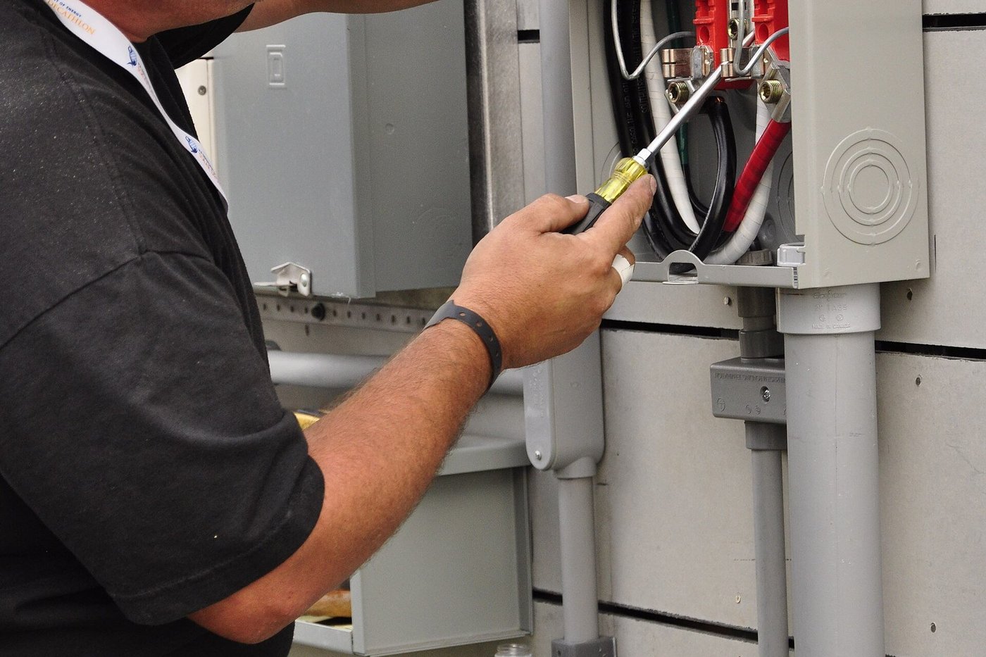 Een elektricien met helm werkt in een schakelkast met gereedschap in de hand.