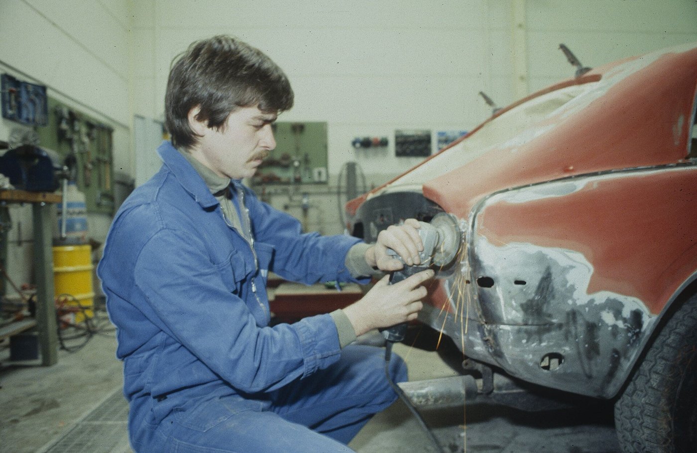 Een historische foto van een leerling-autoplaatwerker die in een werkplaats een autodeur bewerkt.