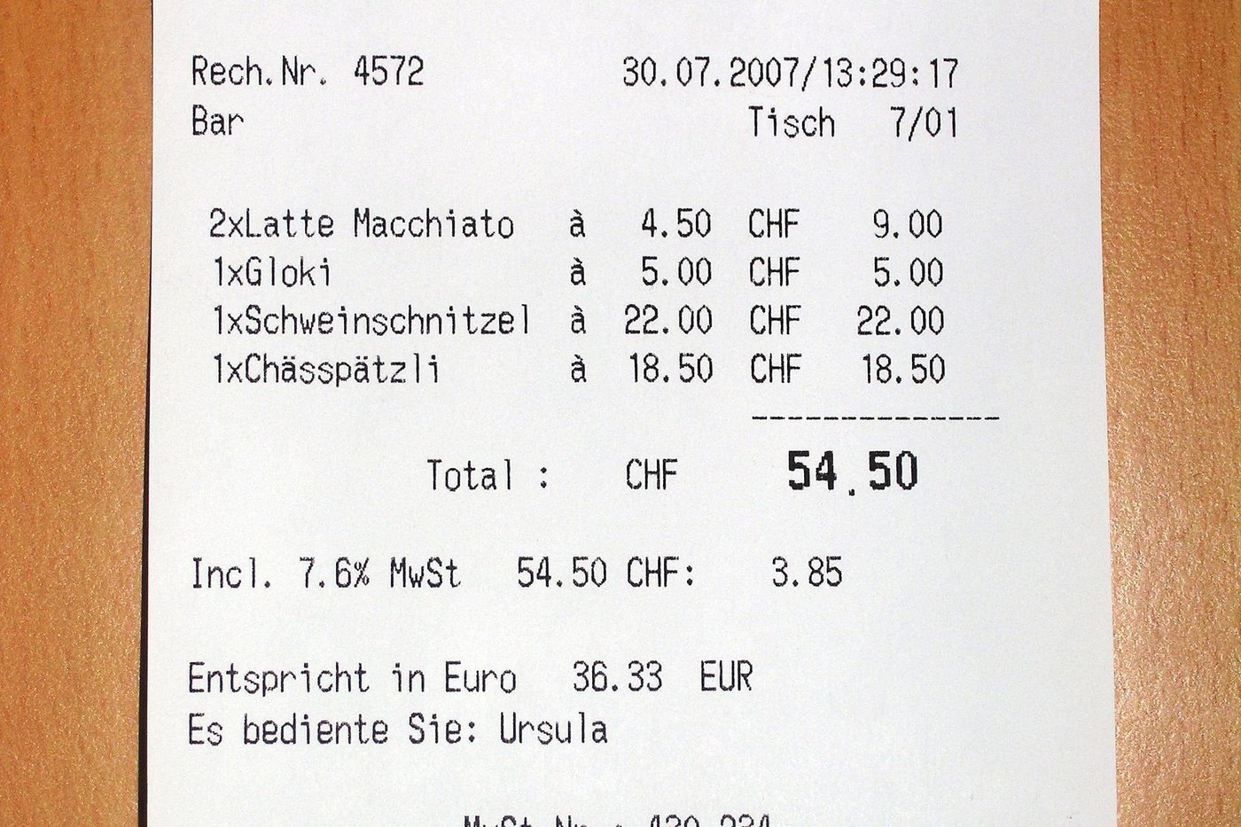 Een kassabon van een restaurant ligt op een houten tafel.