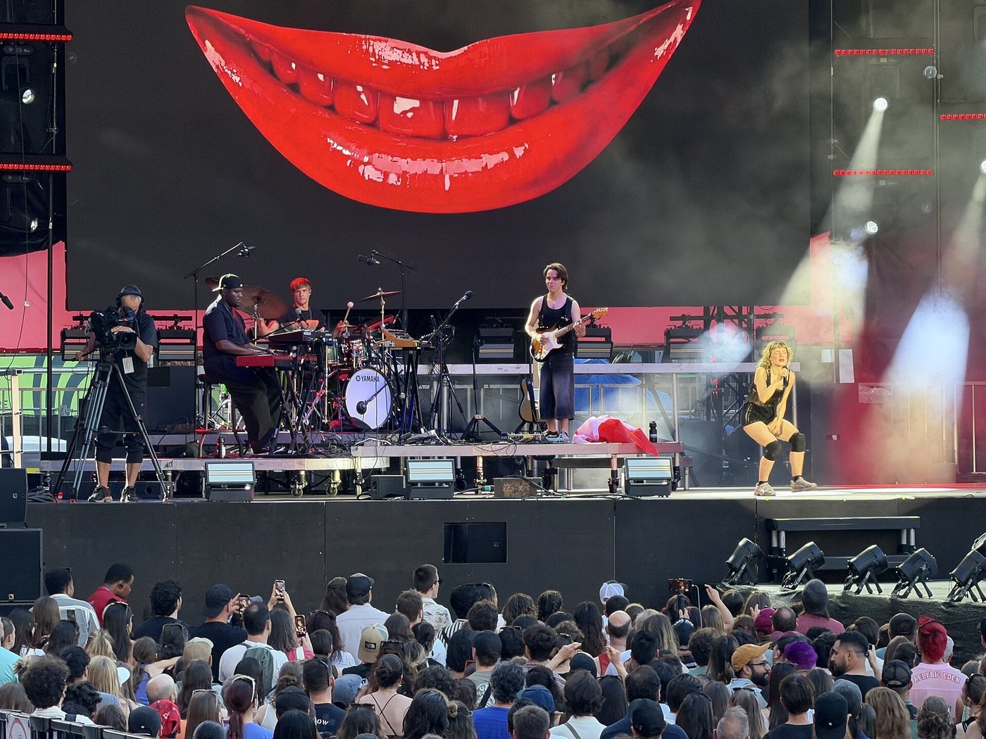 Een festivalpodium met een band en een volle menigte ervoor in de avond.