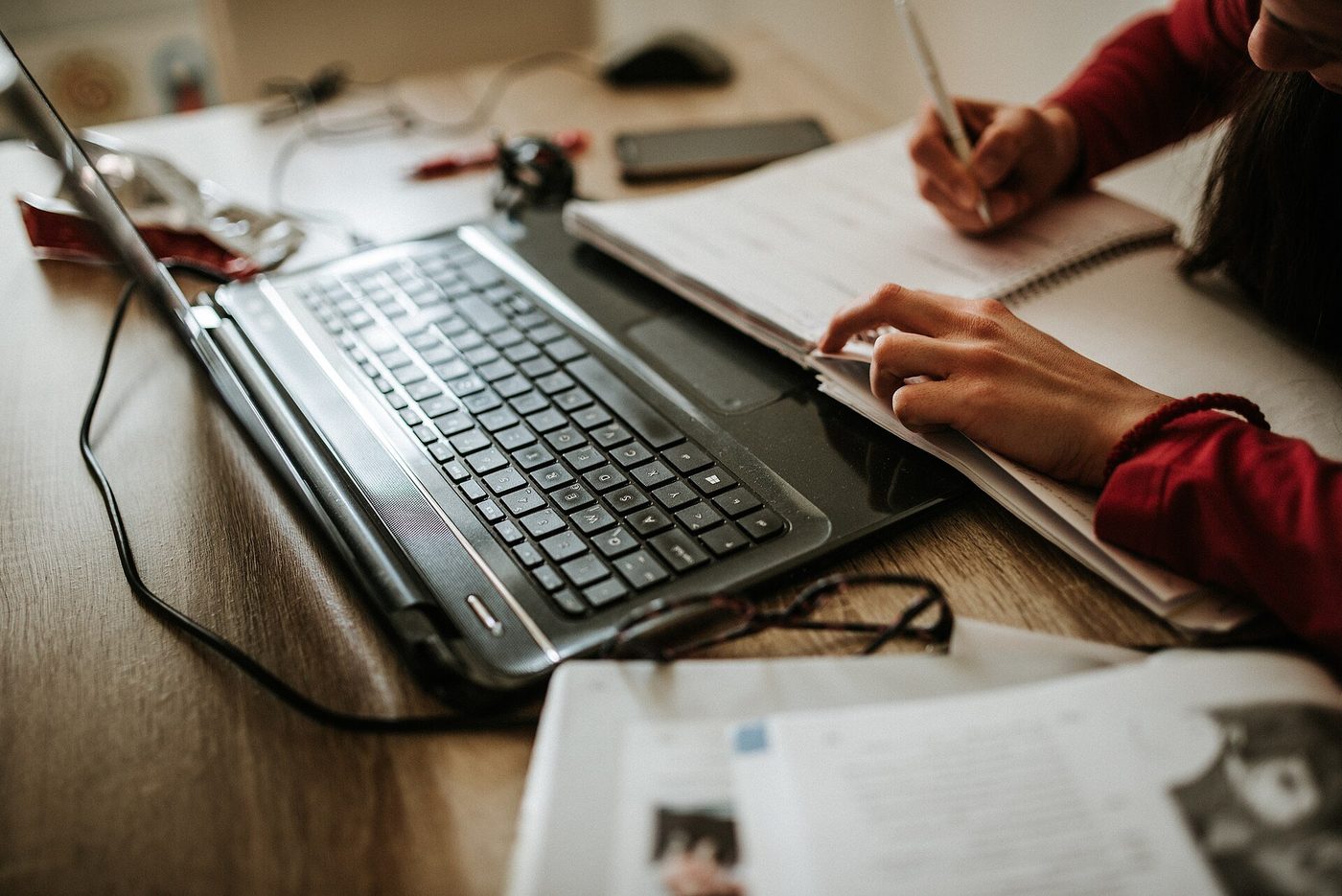 Iemand werkt thuis aan een laptop met een notitieboek ernaast.