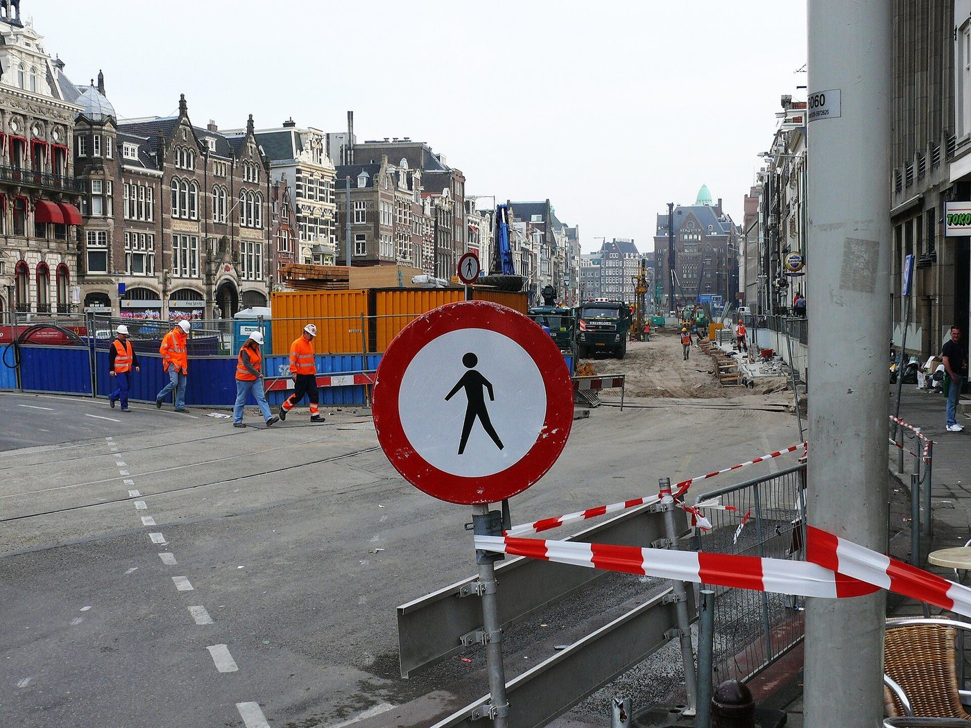 Bouwvakkers in oranje hesjes lopen over een afgezette straat bij een bouwput in Amsterdam.