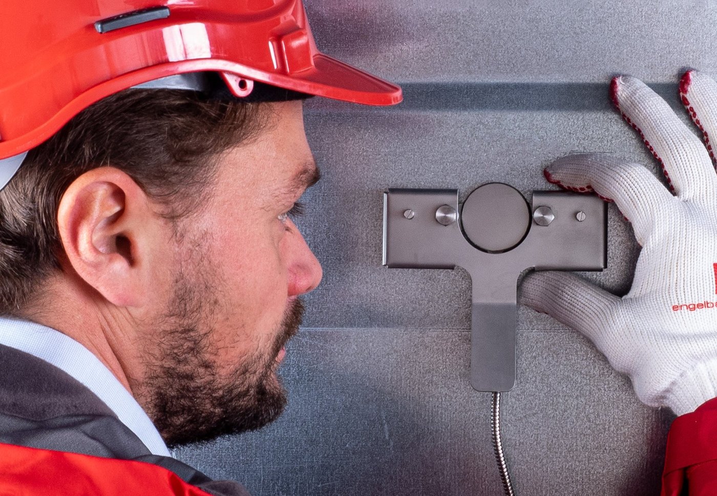 Een monteur met helm en handschoenen monteert een sensor op een metalen wand.