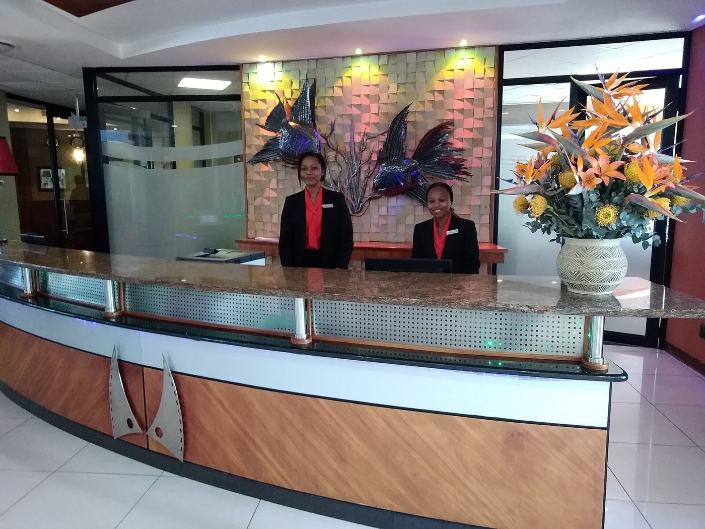 Twee medewerkers achter een receptiebalie in een hotellobby.