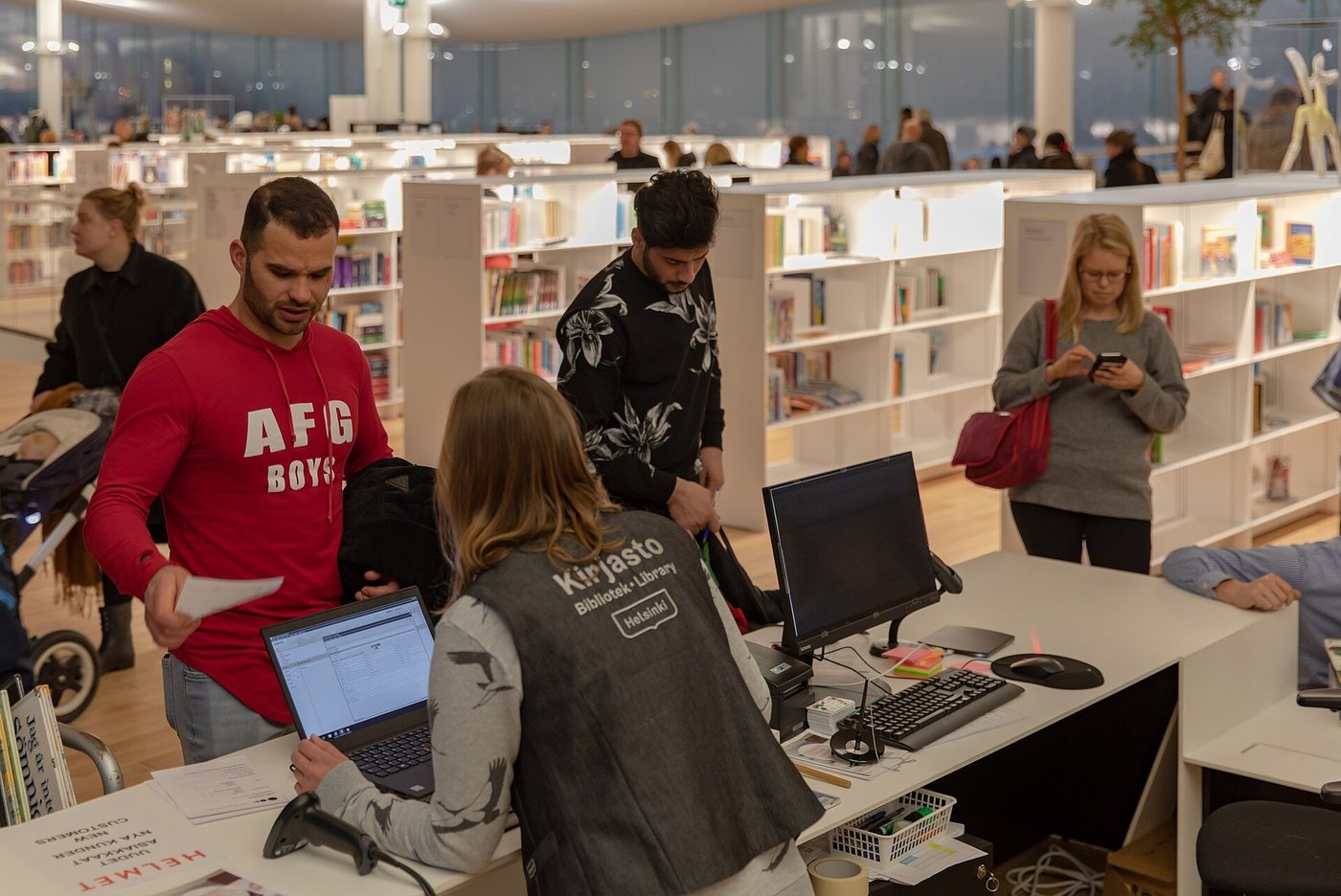 Medewerkers helpen bezoekers aan een informatiebalie met computers.
