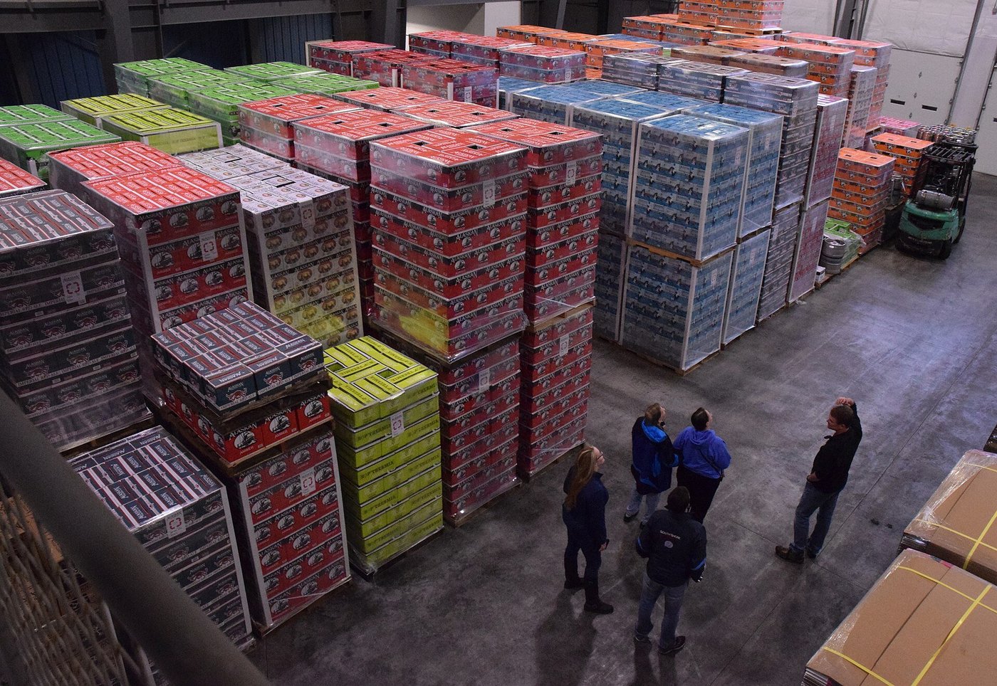 Medewerkers in een magazijn tussen stapels kratten en pallets.