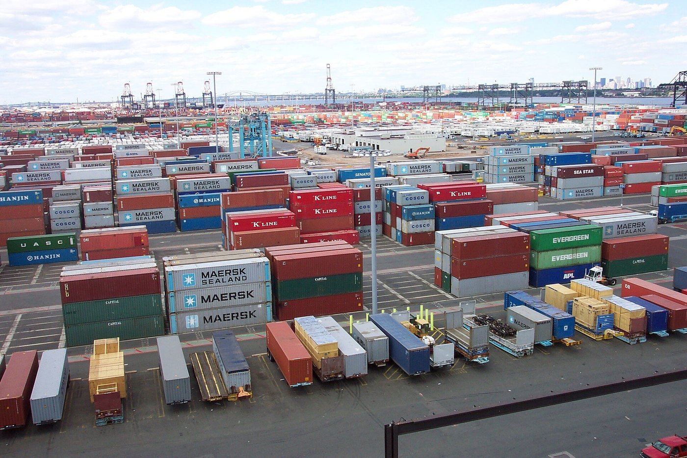 Rijen zeecontainers op een terminal met vrachtwagens ertussen.