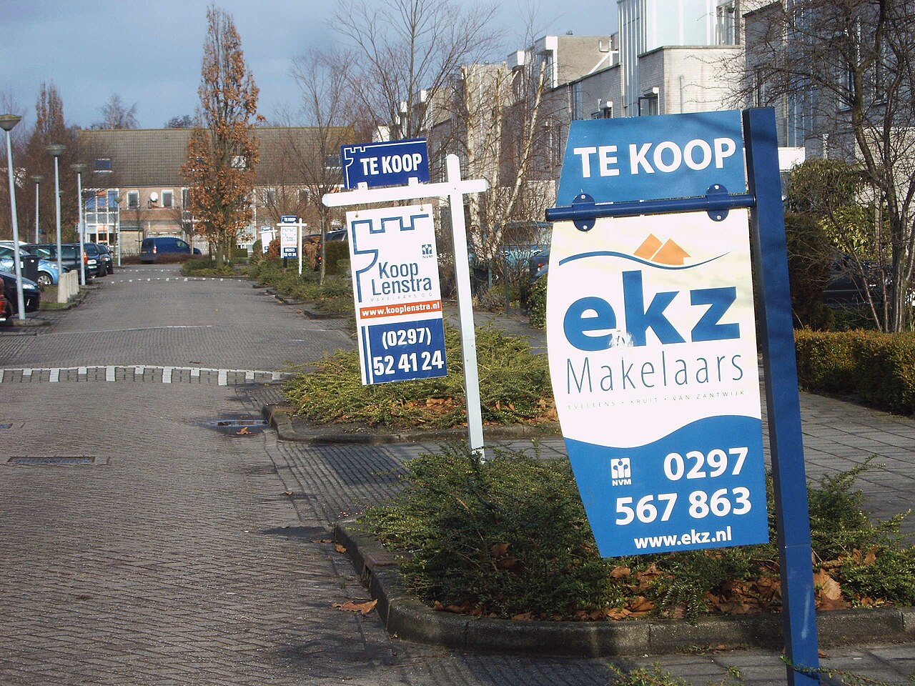 Nederlandse rijtjeswoningen met meerdere te-koop- en makelaarsborden in de voortuinen