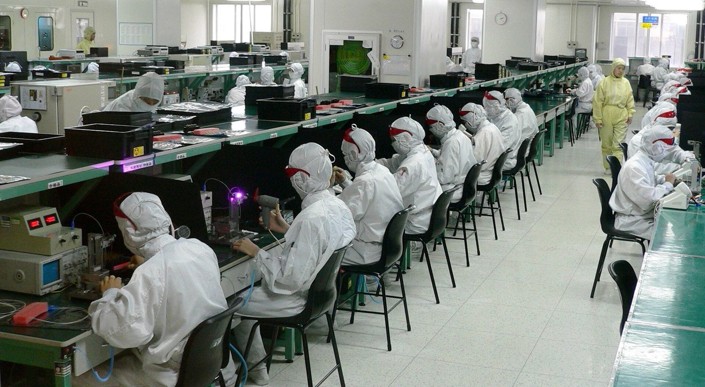 Een productiehal met lange rijen werkplekken en medewerkers aan het werk.