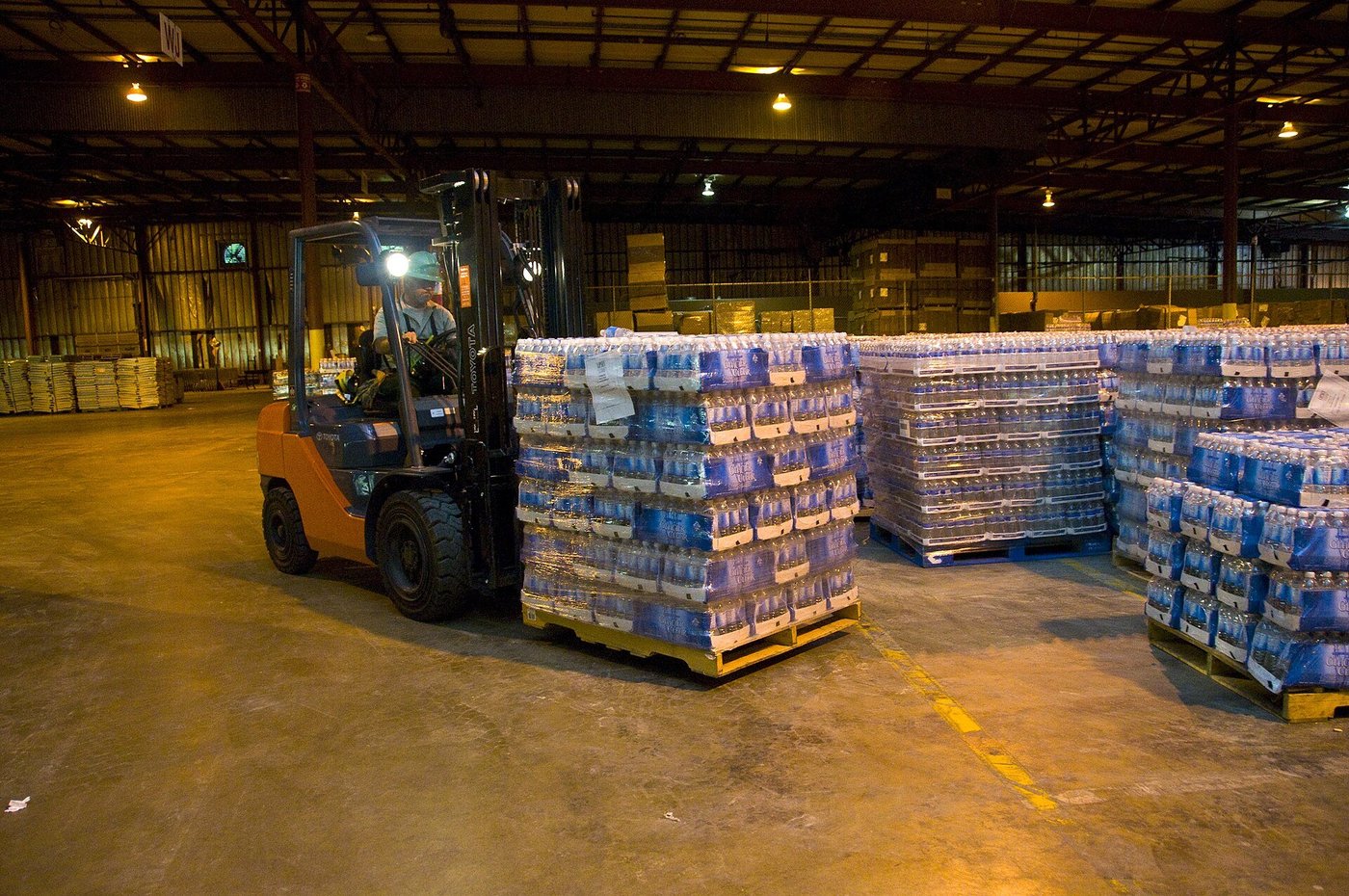 Medewerkers in een magazijn zetten pallets met water klaar met een heftruck.