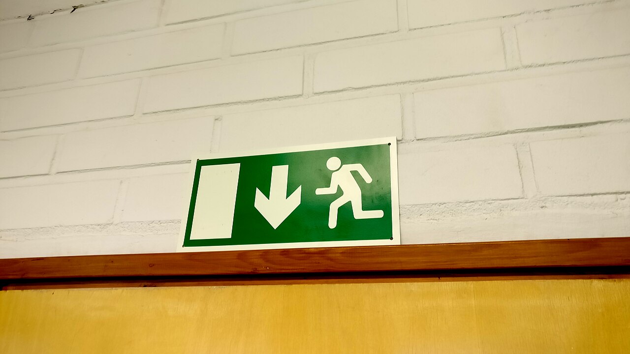 Groen nooduitgangbord met het hardlopende figuur en pijl boven een deur