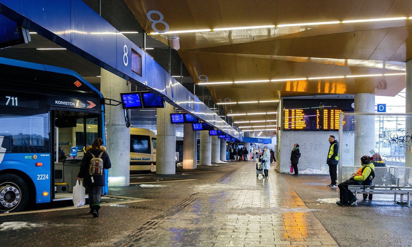 Een overdekt busstation bij een treinstation met bussen op de perrons en reizigers die wachten.