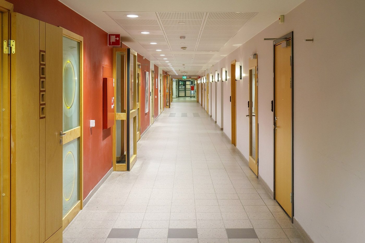 Een lange, lichte gang in een ziekenhuis met deuren aan weerszijden.