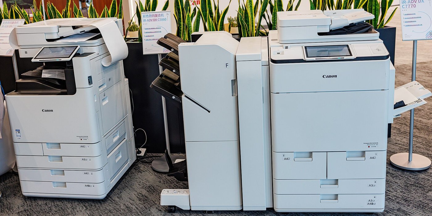Twee grote multifunctionele kantoorprinters naast elkaar op een beursvloer.