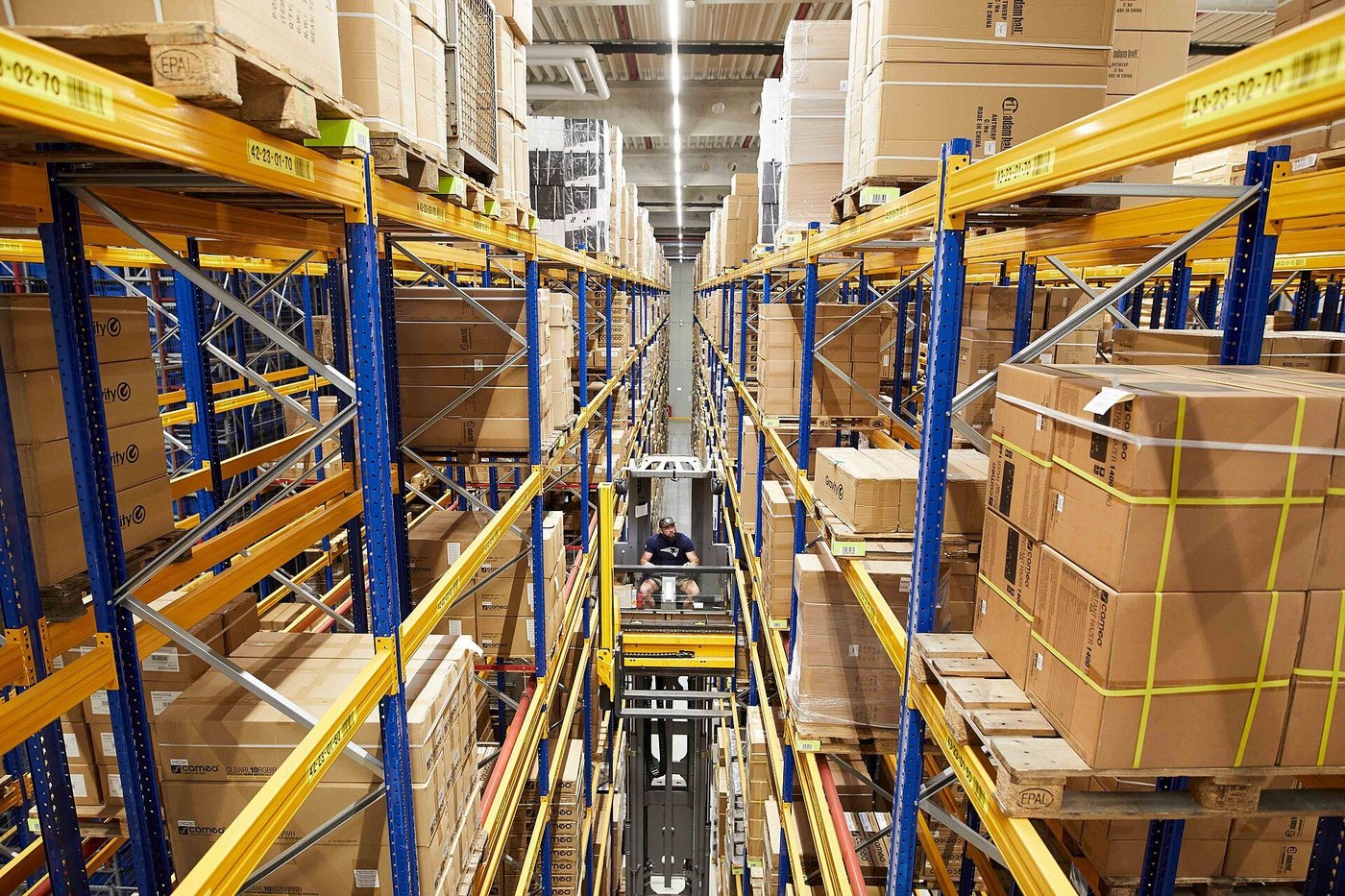 Een magazijngang met stellingen vol kartonnen dozen op pallets.