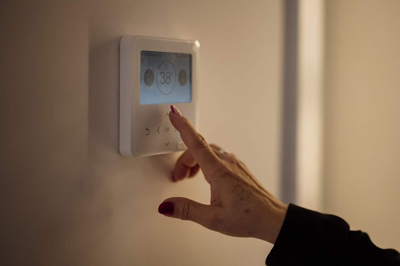 Een hand stelt een thermostaat aan de muur bij.
