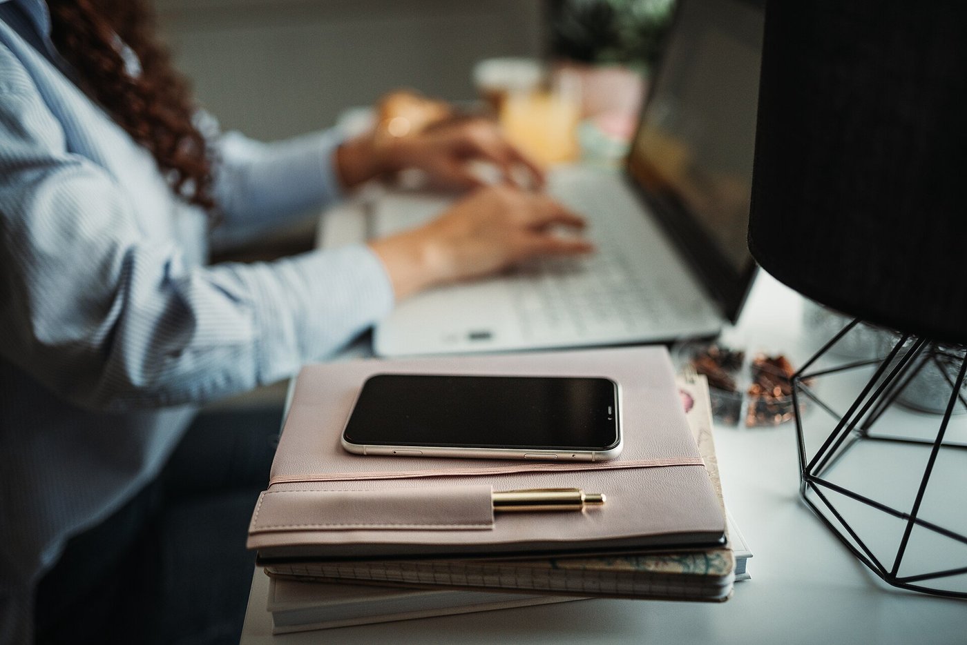 Handen die typen op een laptop op een bureau, met een planner en een telefoon ernaast.