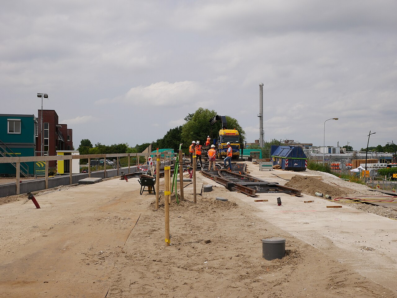 Ploeg infrawerkers in oranje veiligheidskleding en witte helmen overlegt op de bouwplaats van de Uithoornlijn