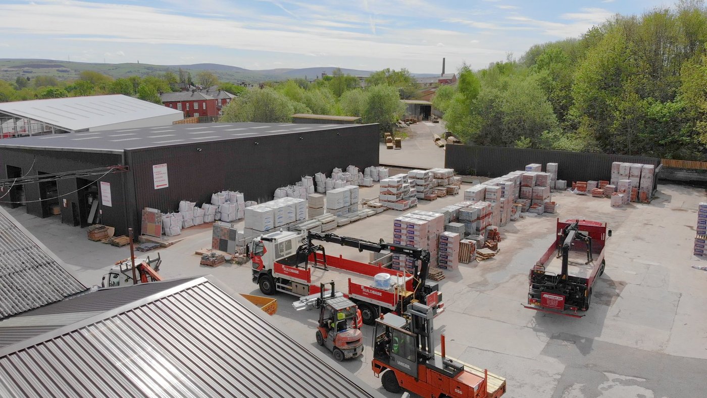 Een buitenterrein van een groothandel met heftrucks tussen gestapelde pallets.