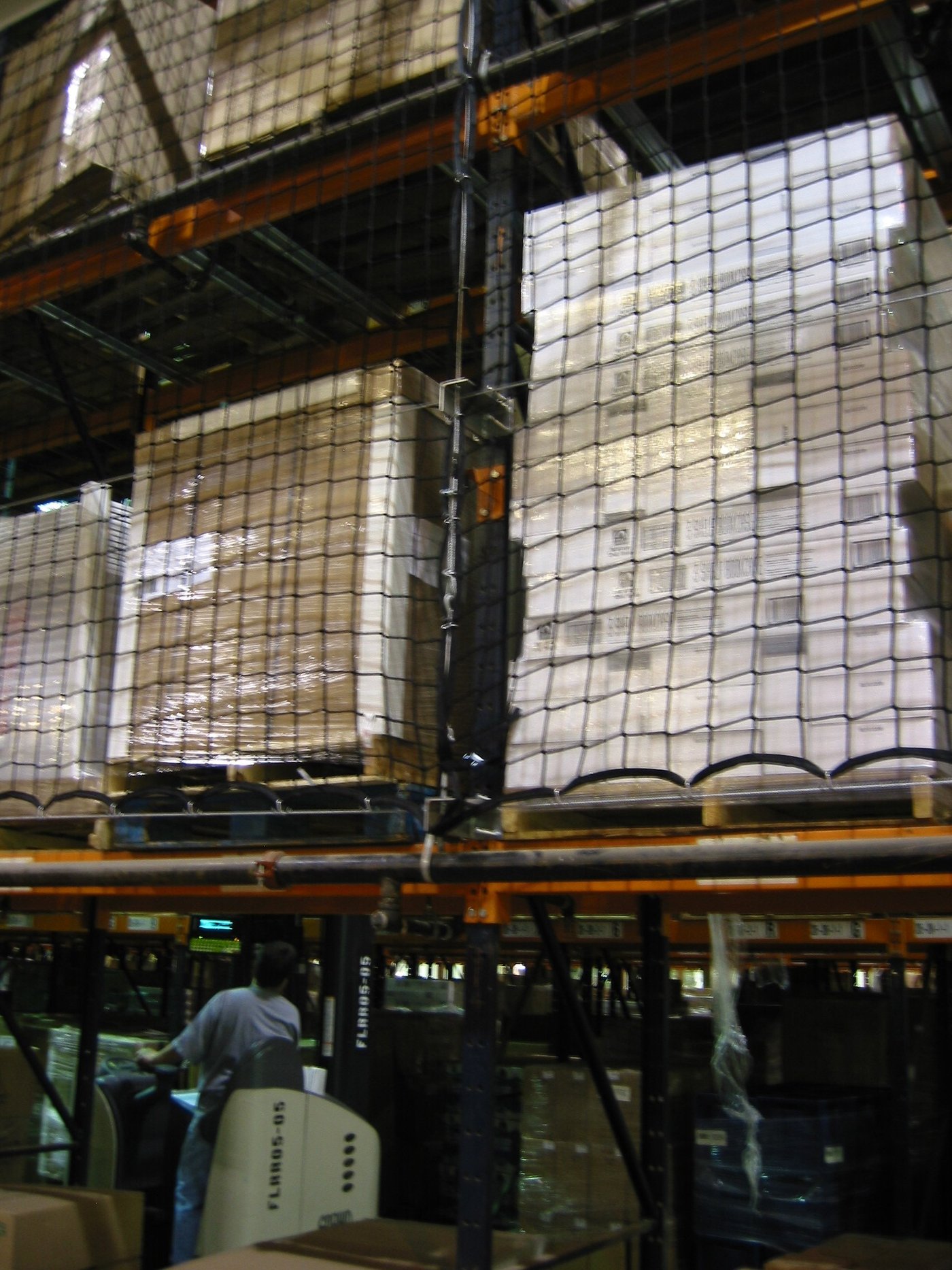 Pallets met ingepakte goederen hoog in een palletstelling, achter veiligheidsnetten.